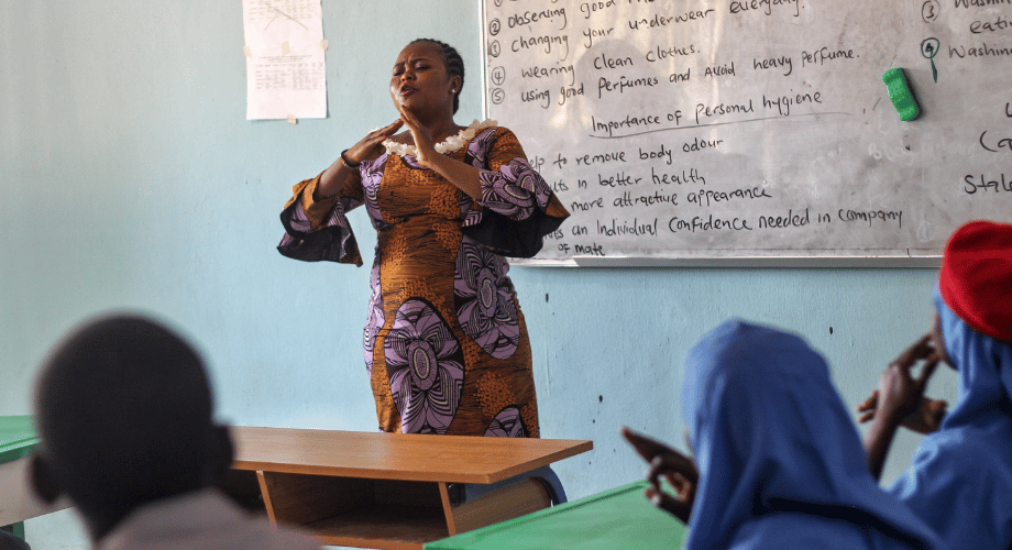 female teacher standing in front of the classroom next to the white board