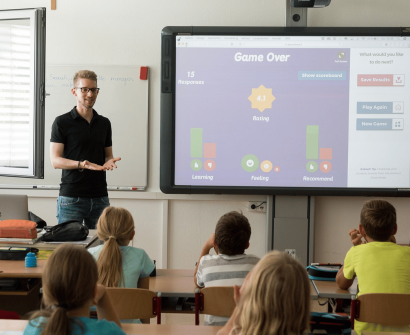 teacher standing in front of the class , learners sitting inside the classroom , big device on the wall